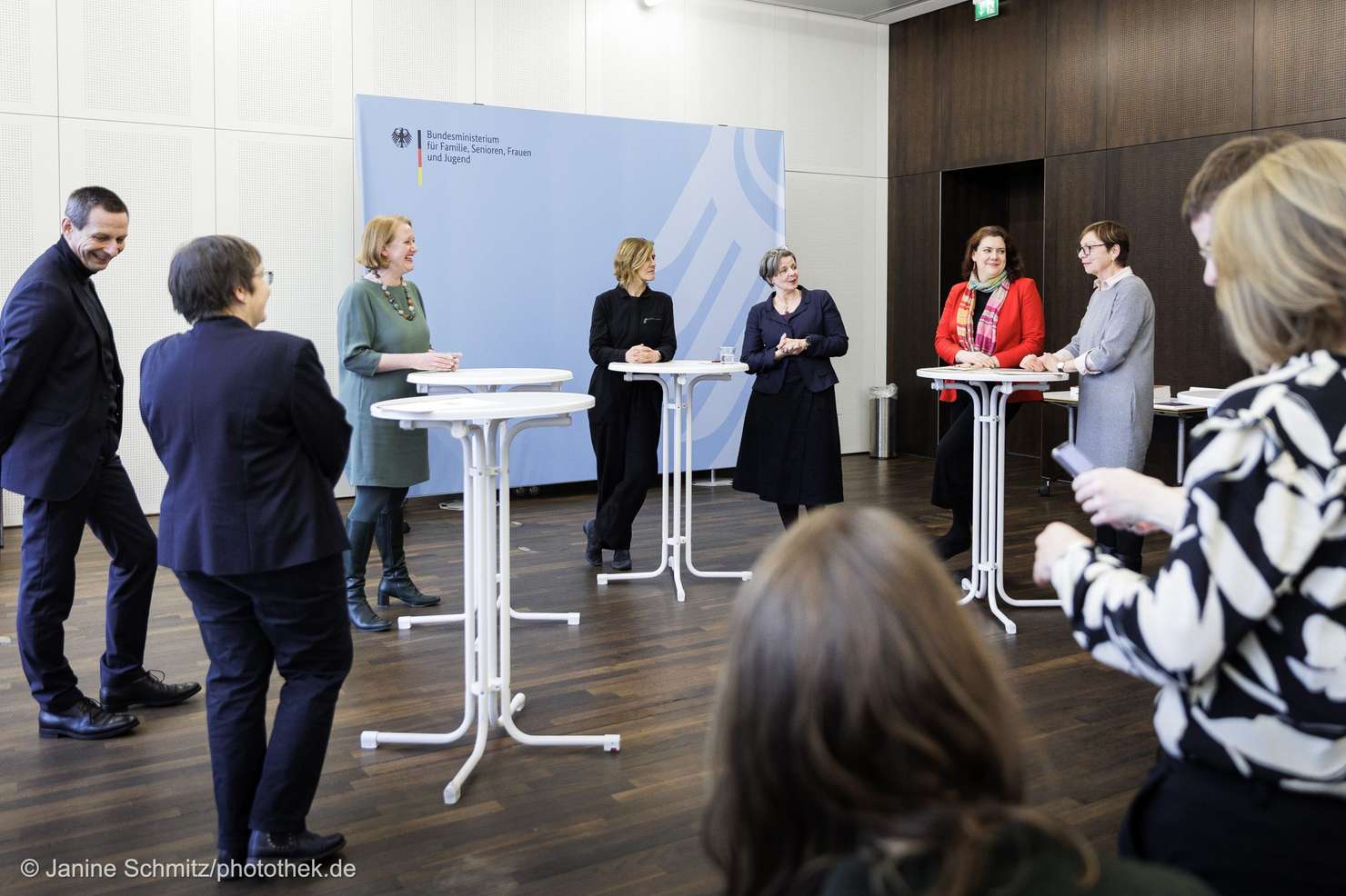 Eine Gruppe von Personen unterhält sich an Stehtischen, vor einem Banner mit der Aufschrift "Bundesministerium für Familie, Senioren, Frauen und Jugend"